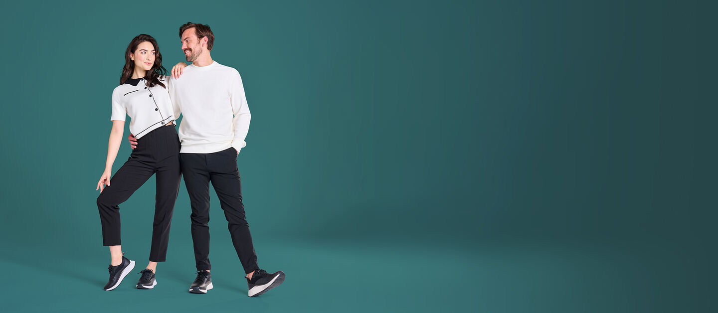 Hombre y Mujer, ambos con blusas blancas y pantalones negros, y el mismo estilo de zapatillas, Tiberia de Negro para ella, Tacoda de Negro para él, cada uno con un zapato de perfil.